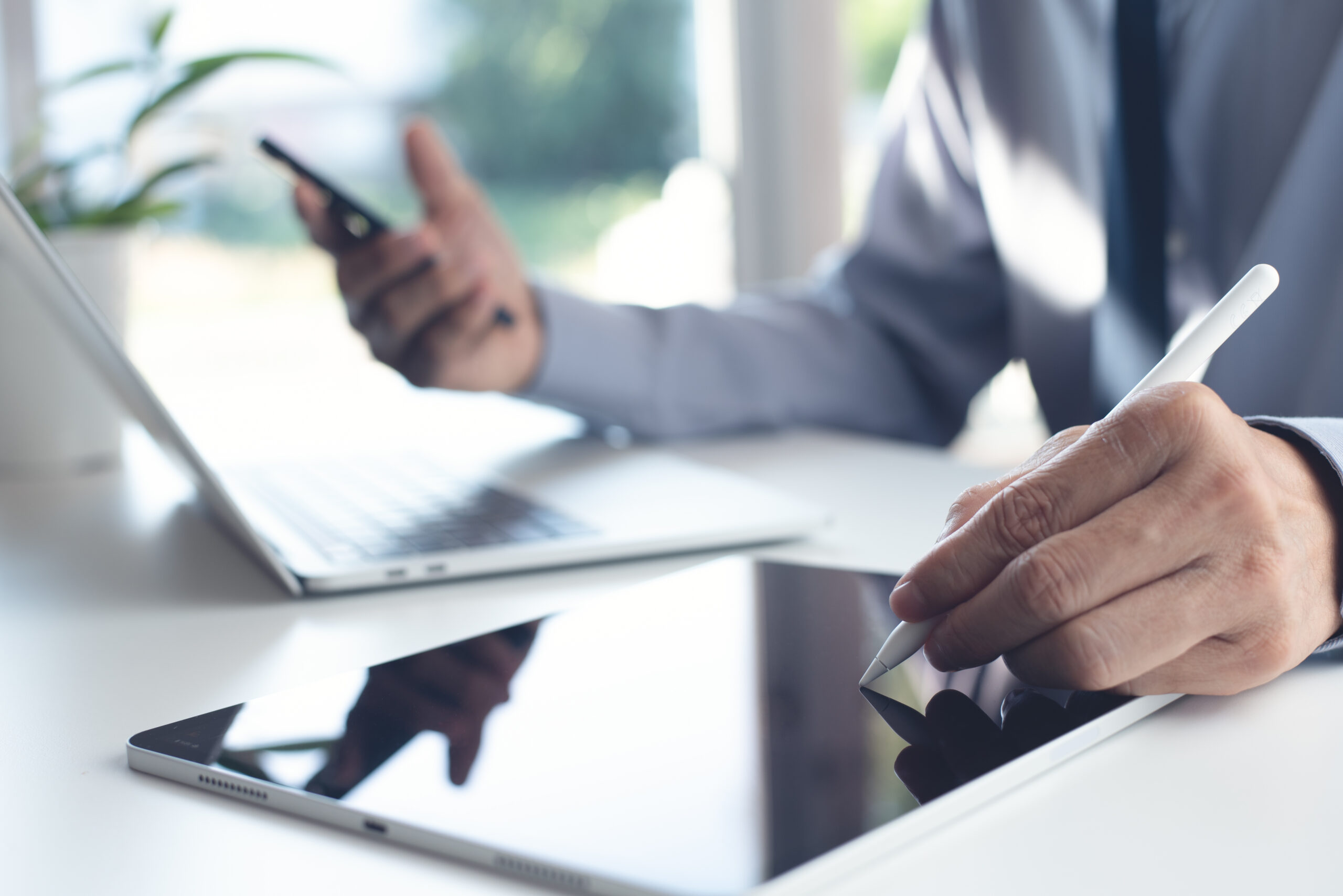 Businessman using stylus pen signing e-document on digital tablet during working on laptop computer and using mobile smartphone on office table