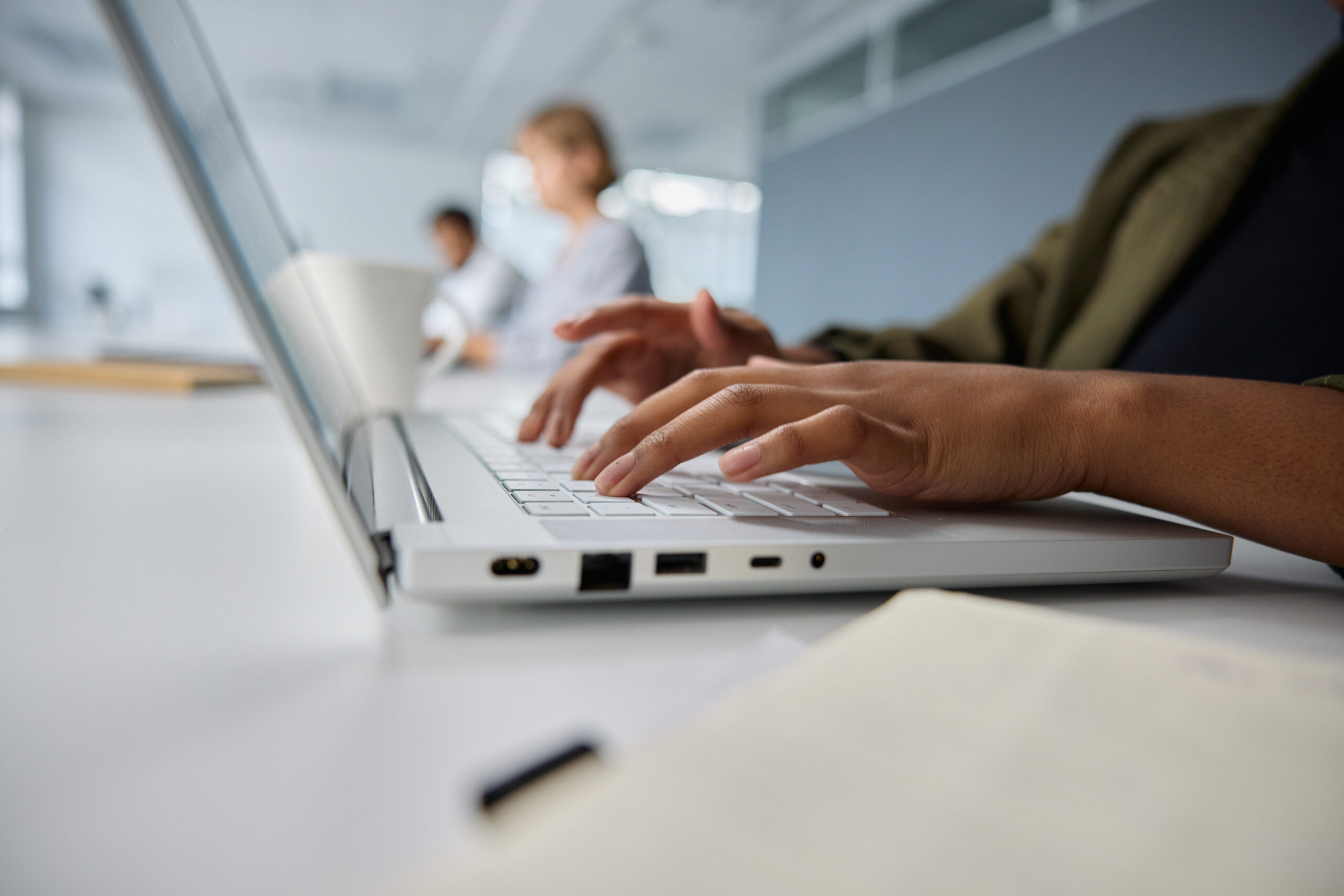 Close-up of three young multiracial business people in businesswear typing on laptop at desk in office