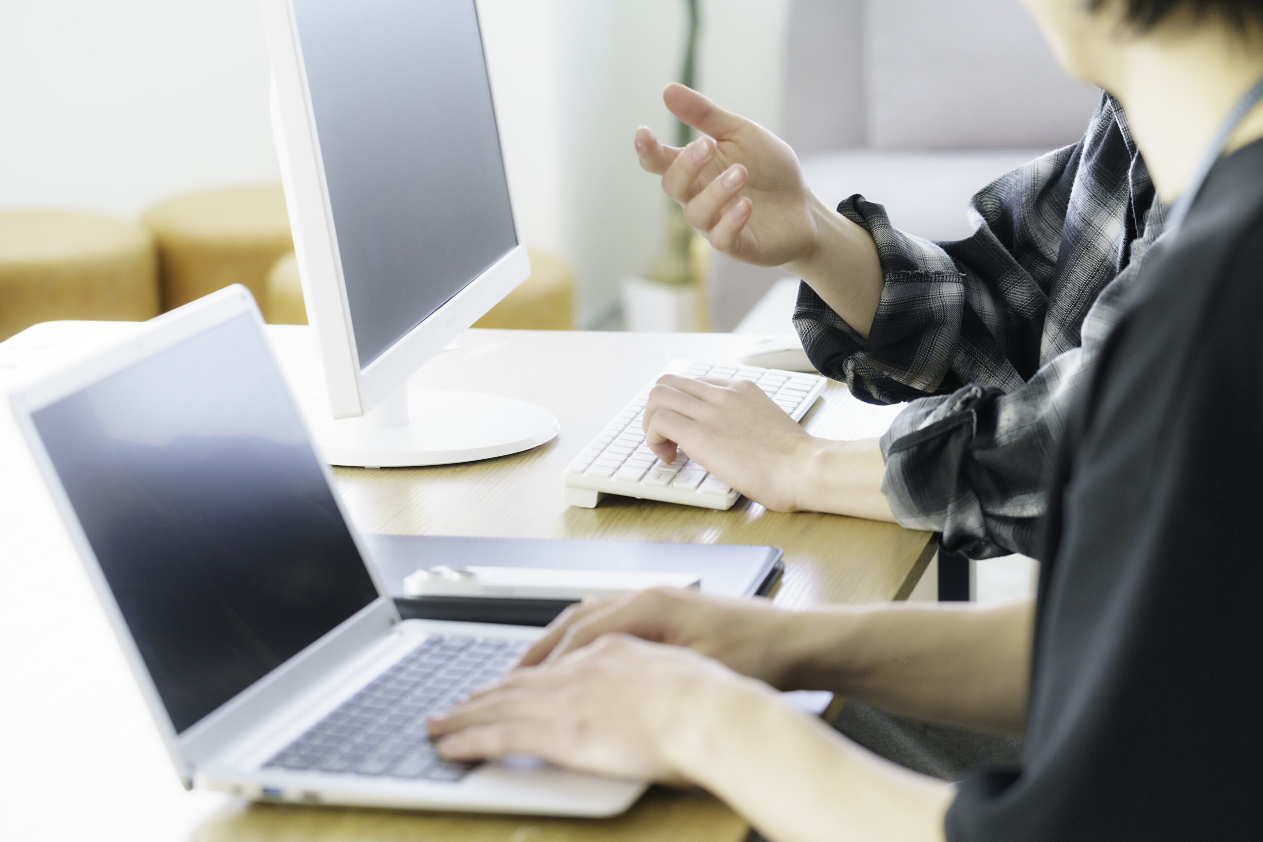 Close-up of the hands of two young Japanese men in casual clothes working on computers in an office.